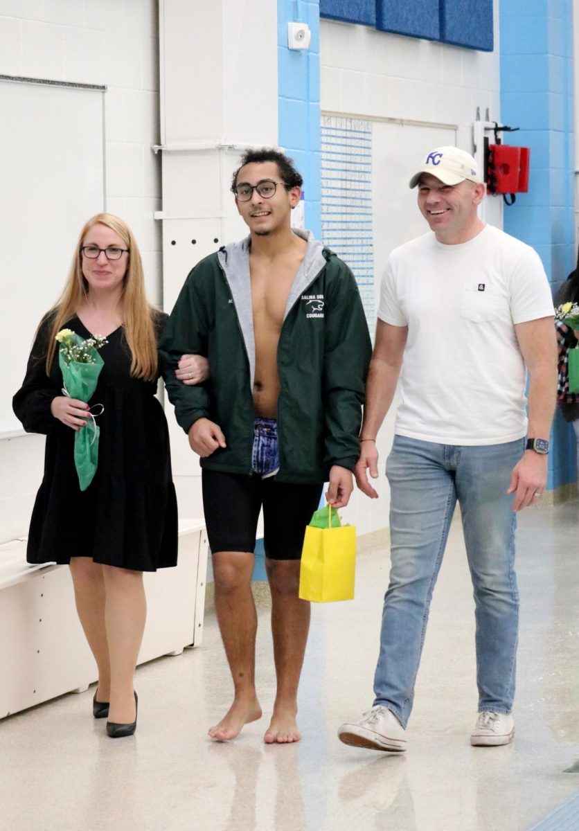 Mason Gardner(24) walks with his parents during the senior recognition portion of the Jan. 31 swim meet. 