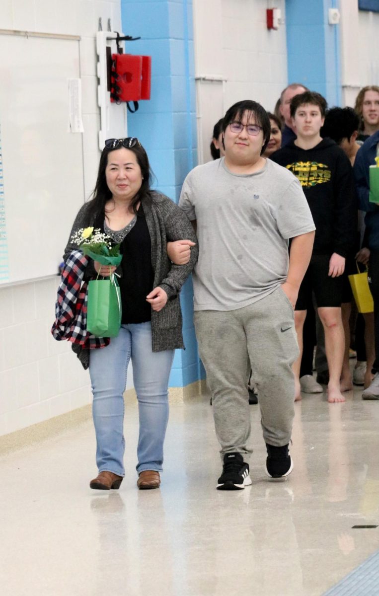 Brandy Huynh(24) walks with his parent during the senior recognition portion of the Jan. 31 swim meet. 