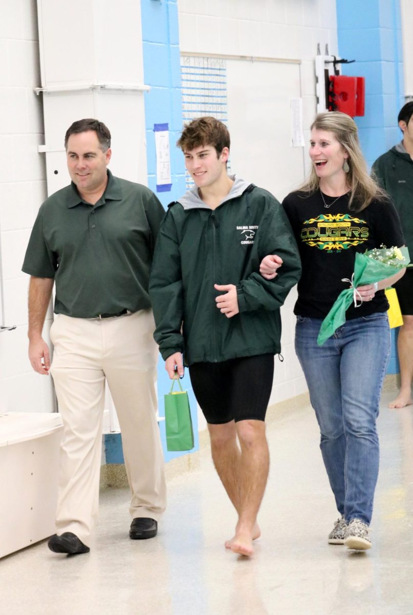 Carson Crow(24) walks with his parents during the senior recognition portion of the Jan. 31 swim meet. 